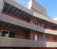Modern multi-story building with orange brick facade, multiple balconies with white railings, and large windows.