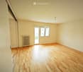 Empty room with wooden flooring, white walls, a radiator, and a large window with a sliding door leading to a balcony.