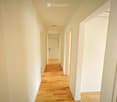 Empty hallway with light wooden flooring, white walls, and several doors leading to other rooms.