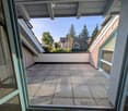 Balcony with tiled floor, glass doors, and a view of trees and neighboring buildings.