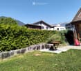 Garden area with a stone retaining wall, a metal fire bowl, and surrounding greenery, with residential houses and mountains in the background.