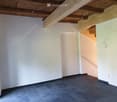 Empty room with exposed wooden ceiling beams, dark tiled floor, white walls, and a staircase leading upwards.