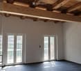 Empty room with exposed wooden ceiling beams, large windows, and tiled floor.