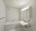 Bathroom with white tiles, white bathtub, white sink, mirror, handrail, shower