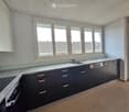 modern kitchen with white cabinets, granite countertops, gas stove, dishwasher, three windows, balcony