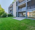 Modern multi-story building with balconies, large windows, and a well-maintained lawn in front.