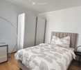 Modern bedroom with a large bed, grey and white bedding, a sleek wardrobe, a desk with a chair, and a floor lamp.