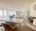 Modern living room with a large window and balcony access, featuring a sofa, coffee table, chairs, a dining table, and a fireplace.