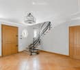 Elegant hallway with a curved staircase, wooden doors, and a chandelier. The space features light grey walls, terracotta tiles, and a decorative ceiling.