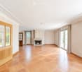 Empty room with beige tiled flooring, white walls, large windows with curtains, and a fireplace with a decorative mantel.