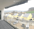 Balcony overlooking a residential area with houses, parked cars, and a rural landscape.