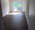 Empty room with wooden flooring and large sliding glass door leading to a view of greenery outside.