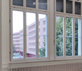 Empty room with large windows, radiators, and a red carpeted floor. No furniture or equipment is present.