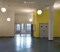 Empty room with polished dark flooring, white walls, and modern lighting fixtures. Features include a large doorway leading to an outdoor area, a yellow accent wall, and a white shelving unit with a few items on it.