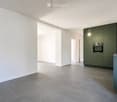 Empty room with grey tiled floor, white walls, and a small kitchen area with green cabinets, sink, and oven.