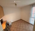 empty room, white walls, wooden flooring, ceiling lamp, desk with monitor, small bench, window with curtains