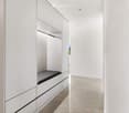 Modern, minimalist hallway with white walls, built-in storage units, and a small bench seat integrated into the cabinetry.