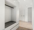 Modern, minimalist hallway with white walls, wooden flooring, built-in storage unit with black seating, and two doors.