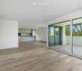 Open-plan space with light wooden flooring, white walls, and a modern kitchen area featuring a kitchen island and cabinets. Large glass sliding doors lead to a balcony with outdoor tiles.