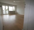 Empty room with wooden flooring, large windows, and a radiator under the windows.