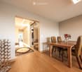 Dining room with wooden floor, dining table, four chairs, vase with flowers, mirror, and decorative shelf.