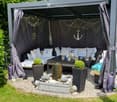A cozy outdoor seating area with a sofa, table, and decorative elements, including potted plants and a small fireplace.
