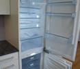 A modern kitchen with a white refrigerator featuring multiple glass shelves and compartments, including a freezer drawer. The refrigerator is open, revealing its interior with clear glass shelves and a few items inside.