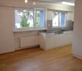 Modern kitchen with white cabinets, black countertop, sink, and radiator under large windows.
