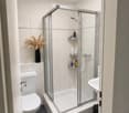 Modern bathroom with a white toilet, a glass-enclosed shower, a sink, and a decorative vase on a shelf.