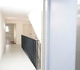 Modern hallway with white walls, light-colored flooring, and a staircase with a black metal railing. An elevator door is visible on the right side.