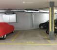 Underground parking area with marked parking spaces, a covered car, a motorcycle, and a storage cabinet.