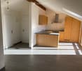 Empty room with tiled floor, white walls, and a doorway leading to a kitchen area with wooden cabinets and a countertop.