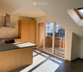 Modern kitchen with light wooden cabinets, stainless steel appliances, and a central island, leading to a balcony with wooden decking.