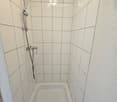 Modern bathroom with a white bathtub, tiled walls, and a handheld showerhead with a handheld shower hose.