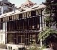 Modern multi-story building with a combination of white walls and dark wooden beams, large windows, and a flat roof with solar panels.