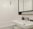 Modern bathroom with white tiled walls, a single sink with a chrome faucet, a large mirror with wooden trim, and a soap dispenser on the counter.