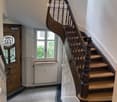 Spiral staircase with wooden steps and ornate balustrade, leading to a landing area with a window and door.