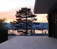 Modern balcony with glass railing, tiled floor, overlooking a scenic view of water and mountains at sunset.