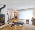 Modern living room with a fireplace, large windows, a sofa, armchair, ottoman, coffee table, and decorative vases.