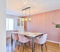 Dining room with a white dining table, pink upholstered chairs, pendant lights, a white cabinet, and a potted plant on a side table.