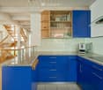 Modern kitchen with blue cabinets, granite countertops, and a coffee maker on the counter. A staircase leads to an upper level.