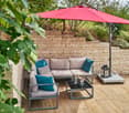 A wooden deck patio with a grey sectional sofa, teal cushions, a black coffee table, umbrella, lantern, and wine bucket.