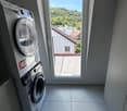 Modern laundry room with a washing machine and dryer, large window offering a view of greenery and neighboring buildings.