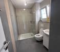 Modern bathroom with a glass-enclosed shower, toilet, sink, and a small window providing natural light.
