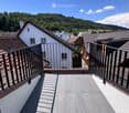 Roof terrace with grey tiled flooring, black metal railing, and scenic view of surrounding rooftops and hills.