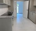 Modern kitchen with light grey cabinets, granite countertop, and a sink with a faucet. An open doorway leads to a tiled area with a view of a balcony.