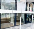 Modern building entrance with large glass doors and a balcony above, featuring signage for "BEAUTY NEL" and website details.