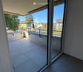 Balcony with tiled floor, glass sliding doors, metal railing, and a view of the surrounding area with trees and buildings.