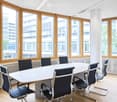 Bright conference room with large windows, a long white table, and several black chairs arranged around it.