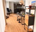 Open-plan living and dining area with light wooden flooring, a sofa, a dining table with stools, a kitchen island, and modern lighting.